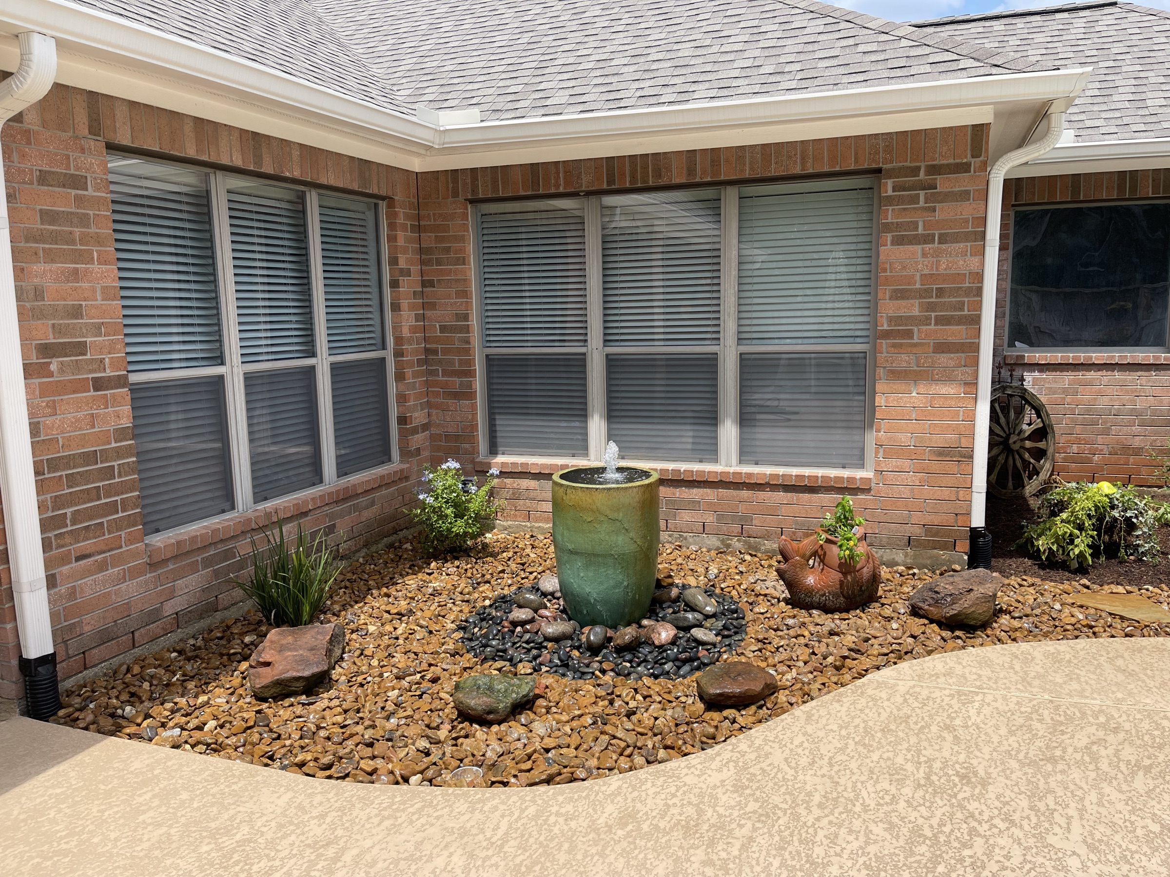 Green urn fountain in a rock bed on a Houston brick home