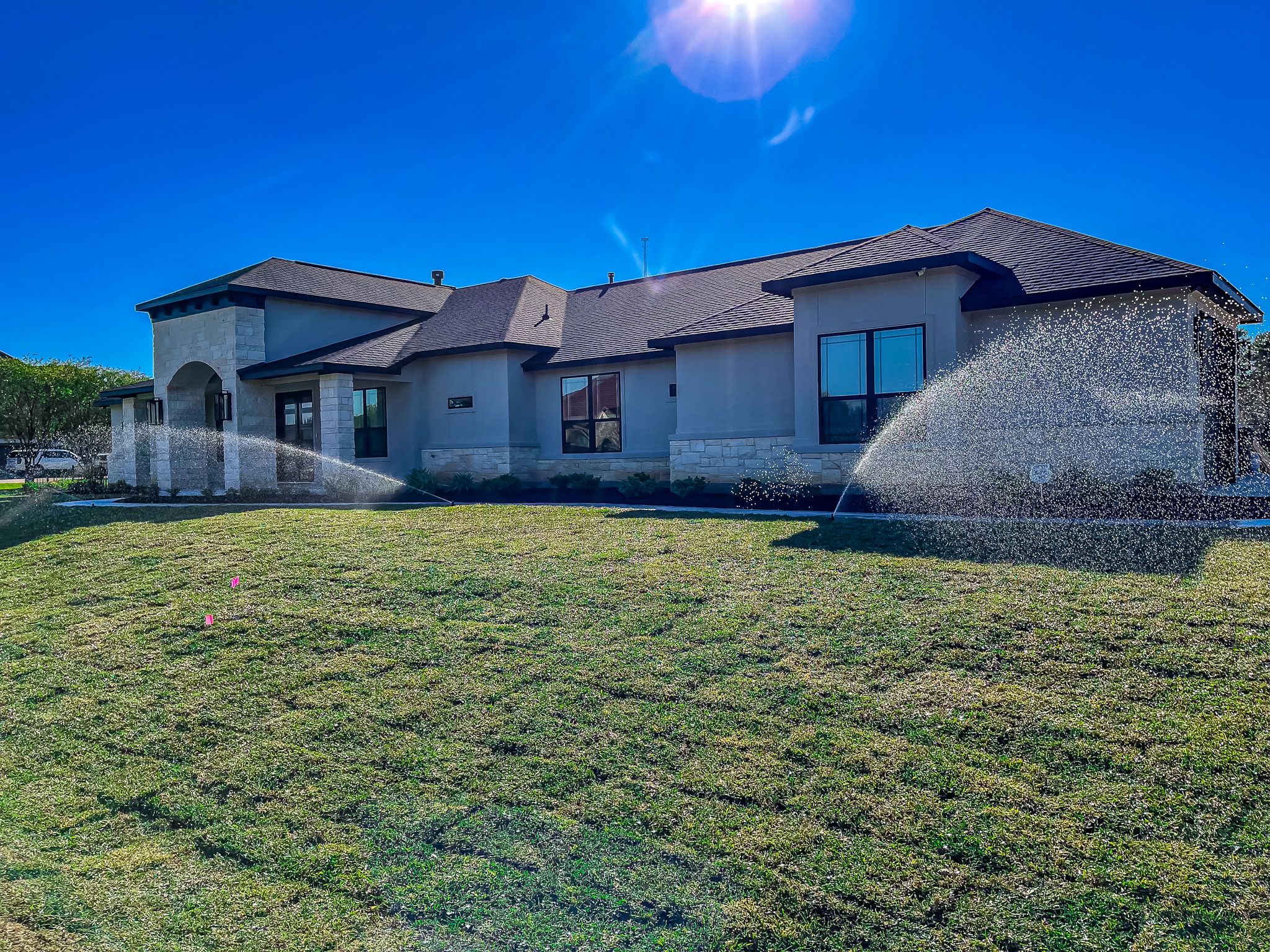 Newly landscaped home with irrigation system watering the lawn, showcasing green grass and modern architecture in a sunny setting, emphasizing quality landscaping services by Danny's Landscaping.