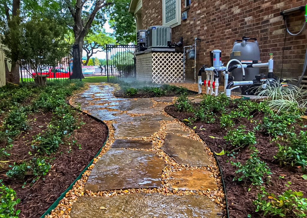Stone pathway winding through landscaped garden with irrigation system, featuring lush greenery and decorative mulch, showcasing professional hardscaping by Danny's Landscaping in Tomball.