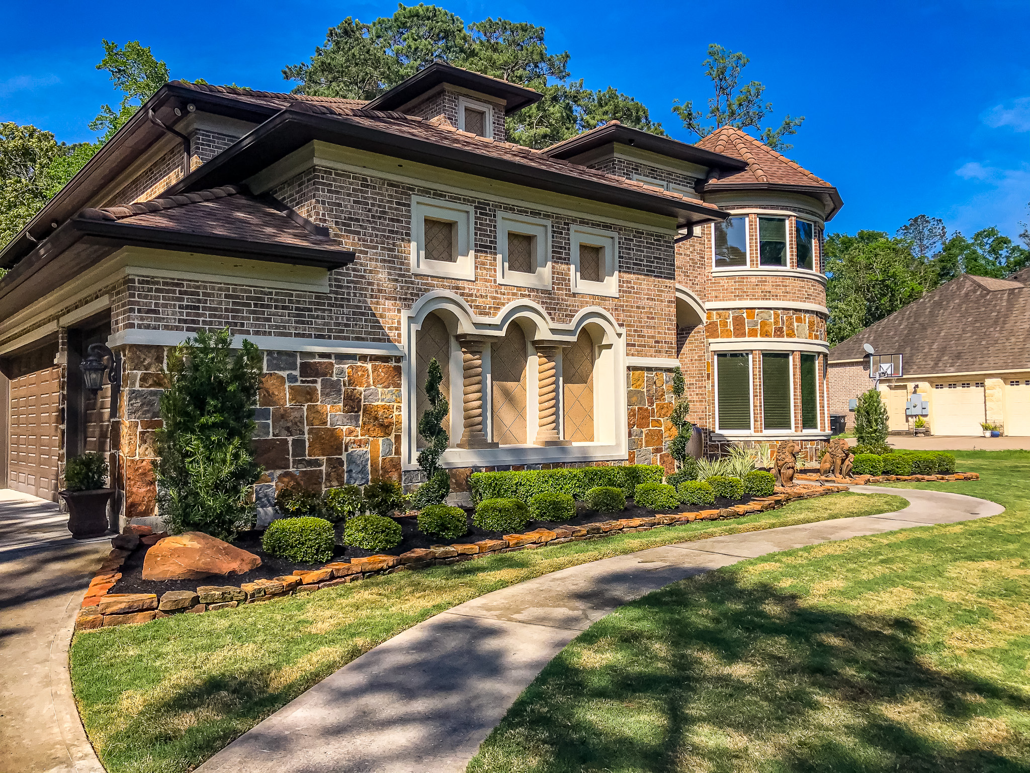Beautifully landscaped home exterior featuring a combination of stone and brick architecture, well-maintained shrubs, and a curved walkway, showcasing Danny's Landscaping expertise in enhancing residential outdoor spaces.