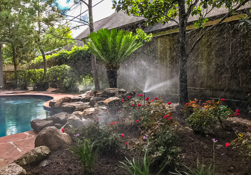 Residential landscaping with a pool, vibrant flowers, and a sprinkler system in a lush garden setting, showcasing Danny's Landscaping expertise in Tomball.